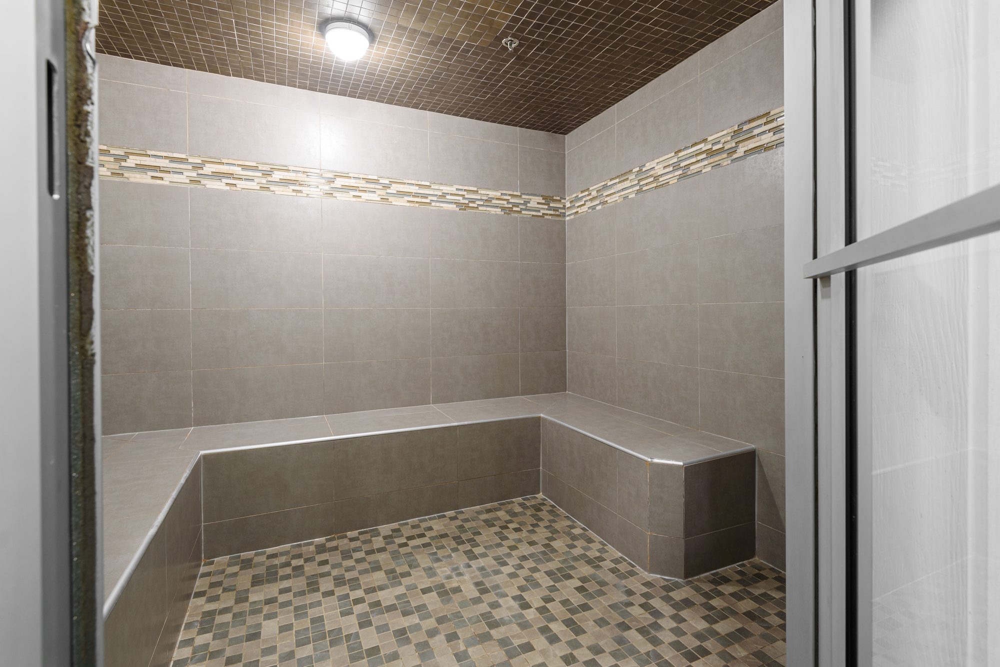 Tiled steam room with bench seating and mosaic accent band