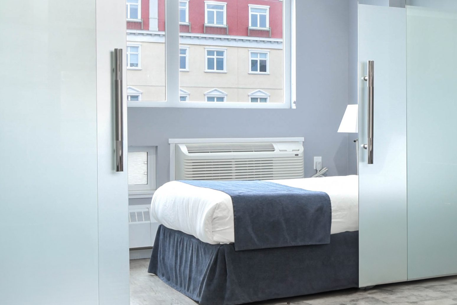 One bedroom with frosted glass partition, made bed, and window view of downtown Regina