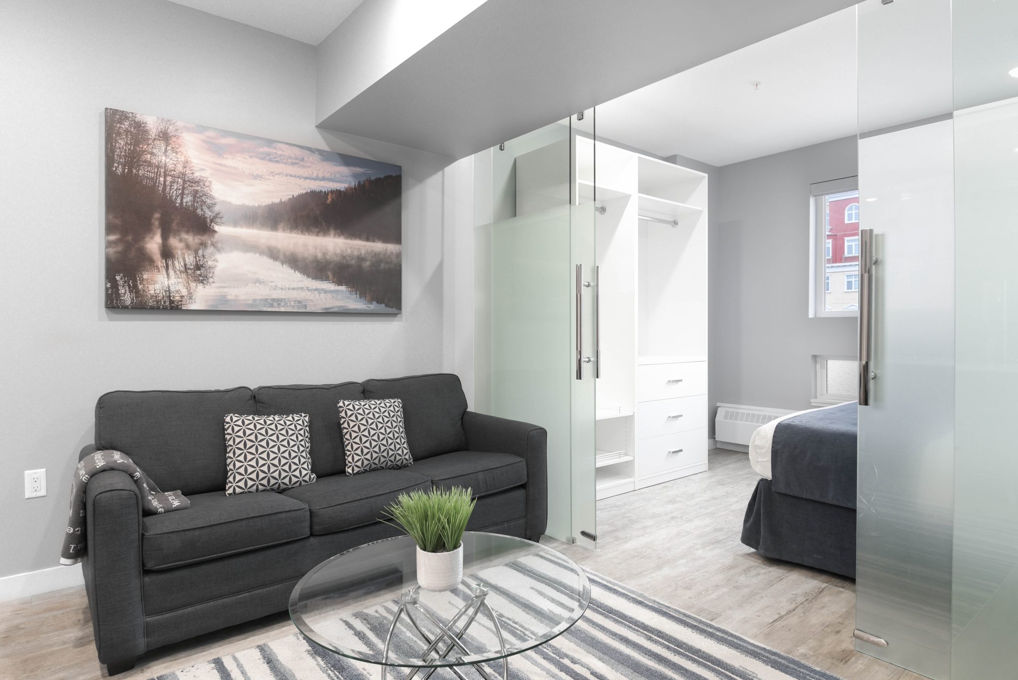 One bedroom living room with grey sofa, glass coffee table, and area rug