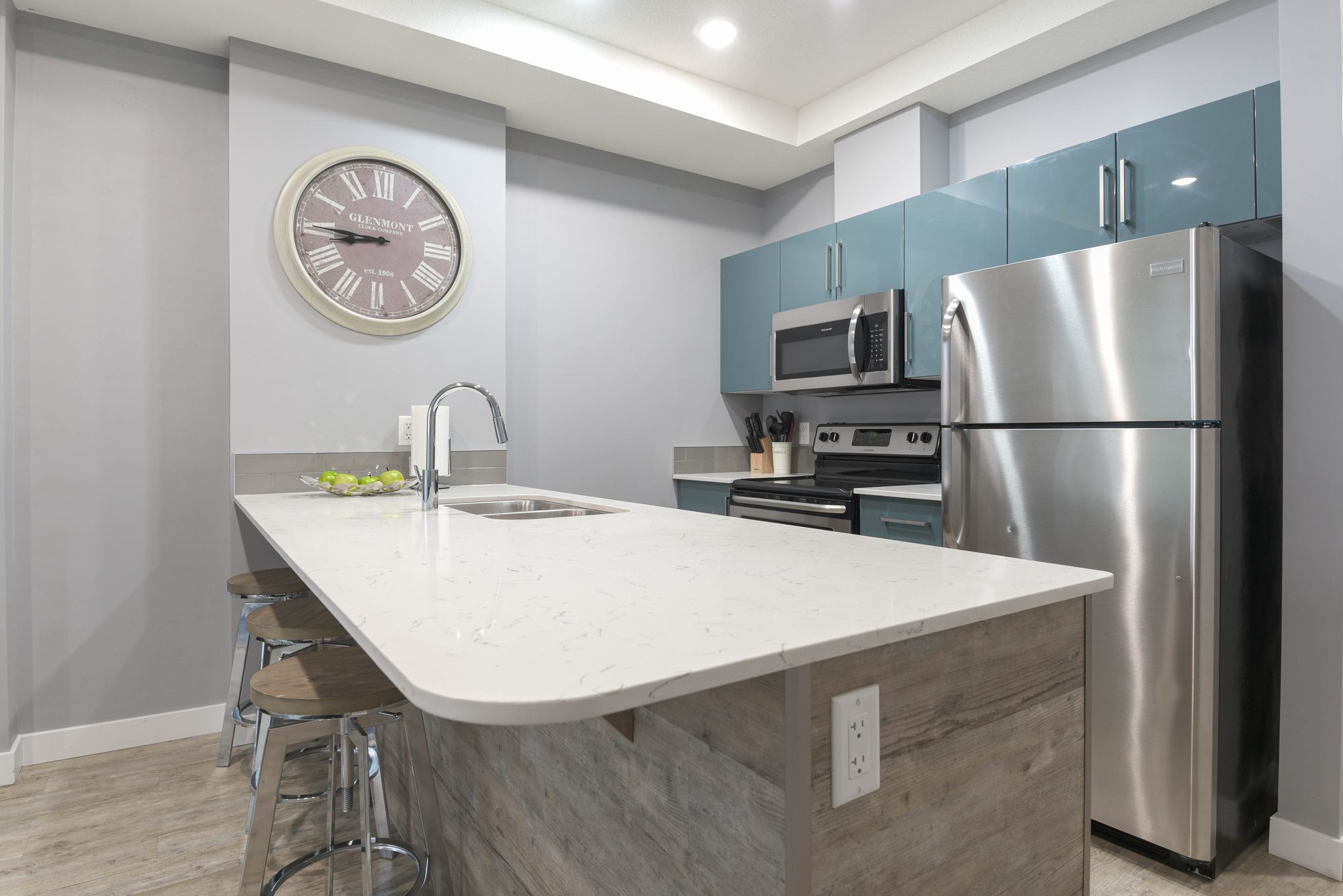 Kitchen island with quartz countertop, stainless steel refrigerator, and teal cabinets