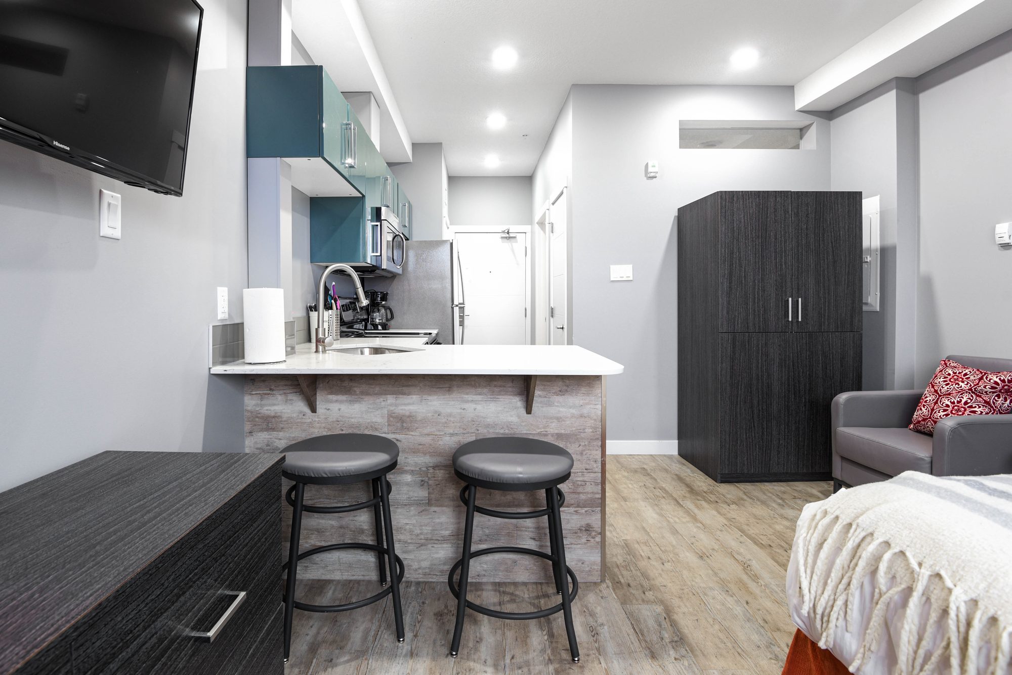 Studio suite kitchen with breakfast bar, two stools, and wall-mounted TV at The Metro 1827