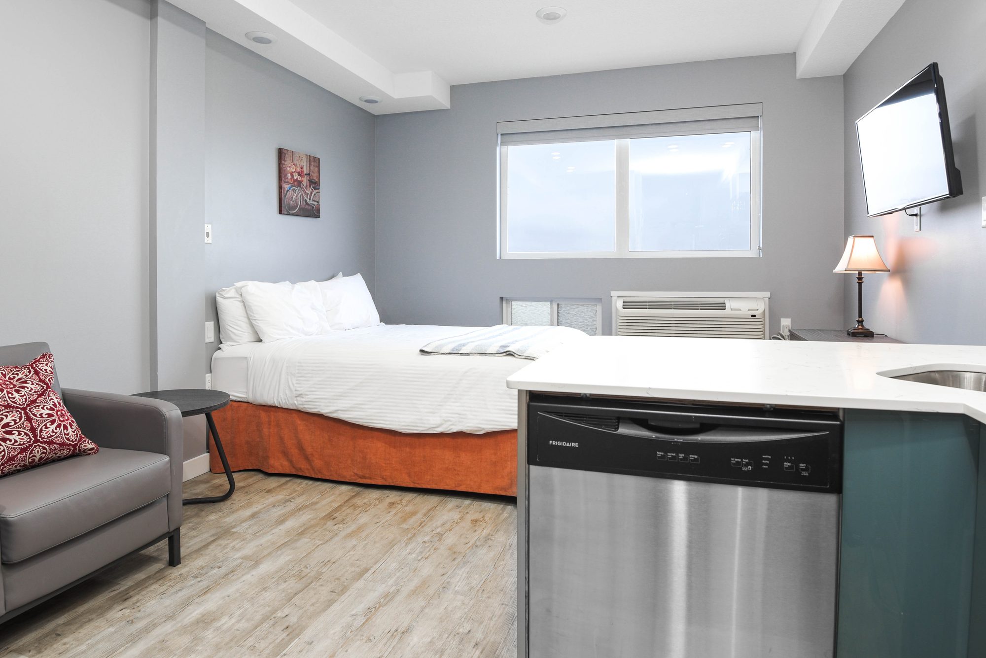 Open studio living area with bed, sofa, and stainless steel dishwasher