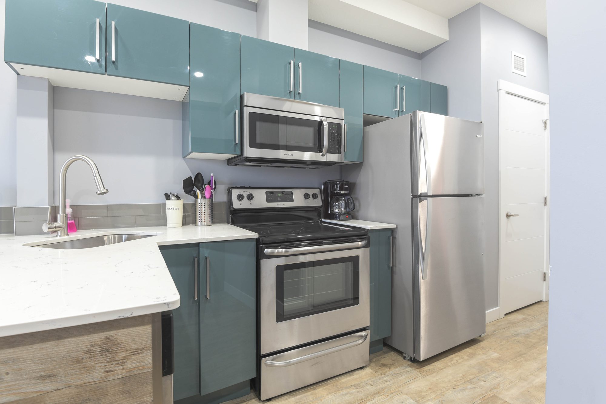 Studio kitchen with teal cabinets, quartz countertops, and stainless steel appliances