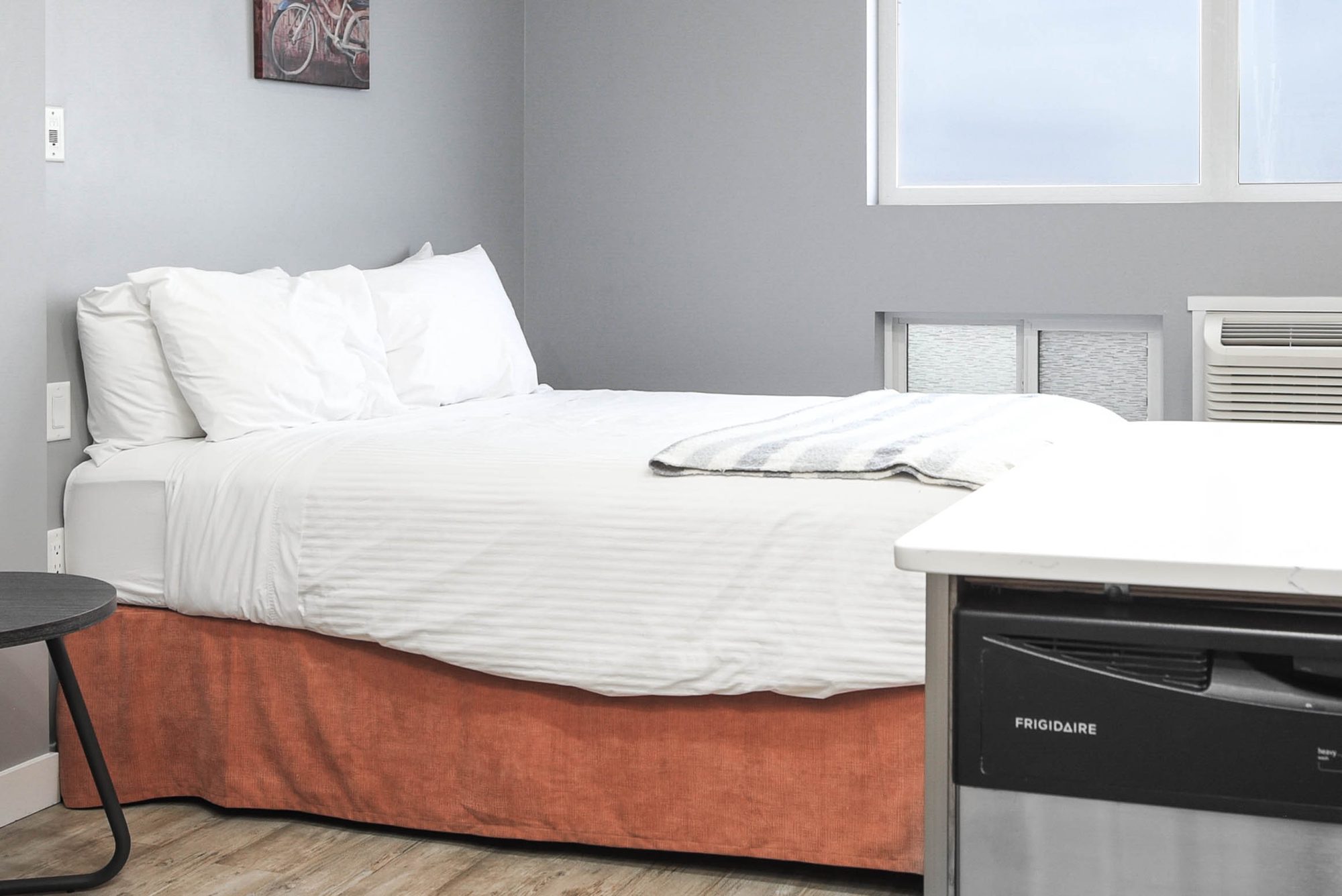 Studio bed beside a bright window with air conditioning unit below